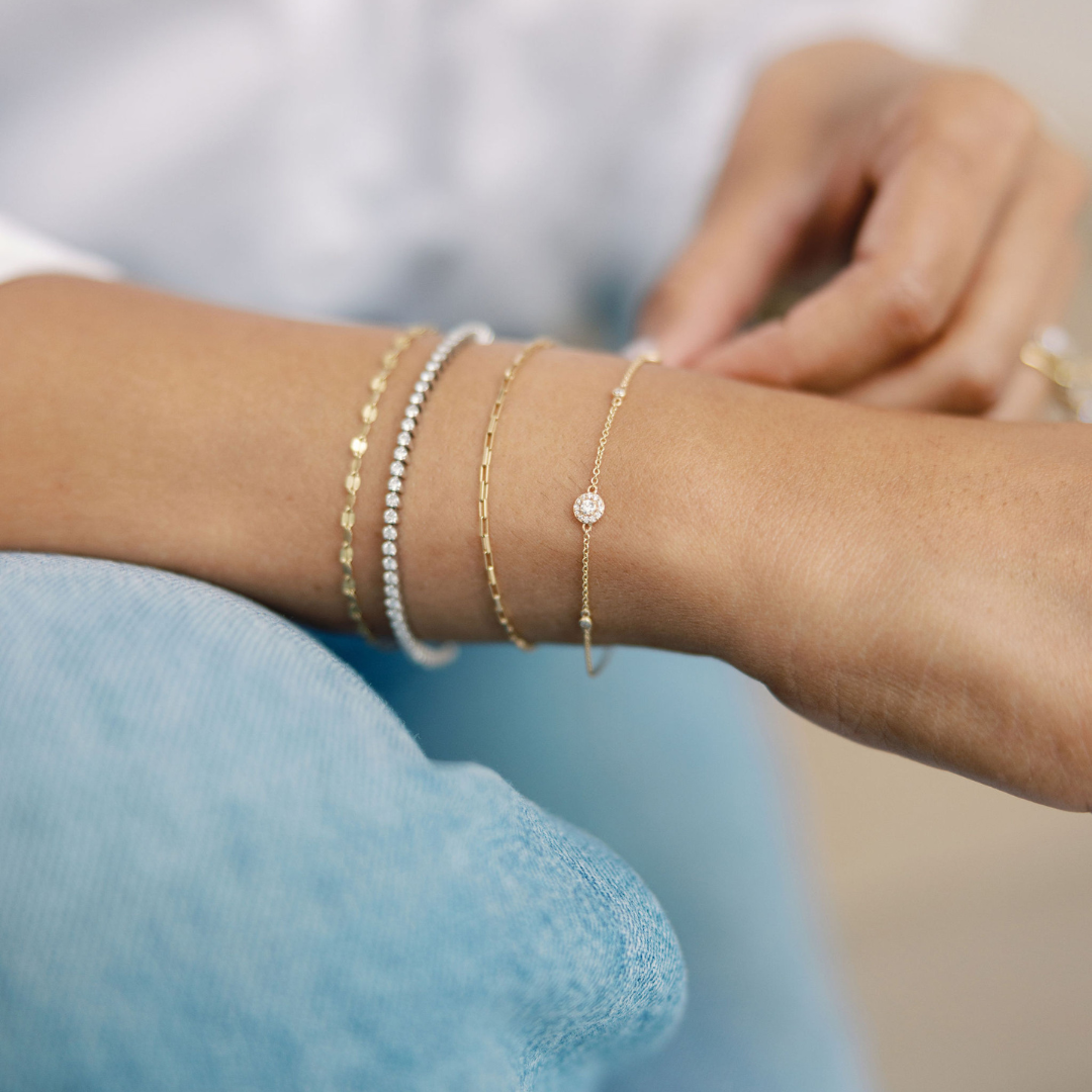 Woman's arm adorned with multiple delicate gold and diamond bracelets, showcasing elegant layering of fine jewelry