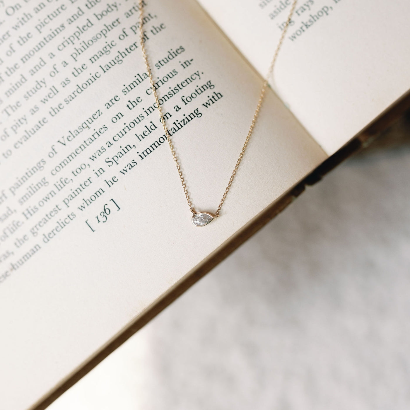 Pear-fect Solitaire Necklace with a lab-grown diamond pendant on a 14K gold chain by Seema Jewelry & Co, elegantly displayed on an open book.