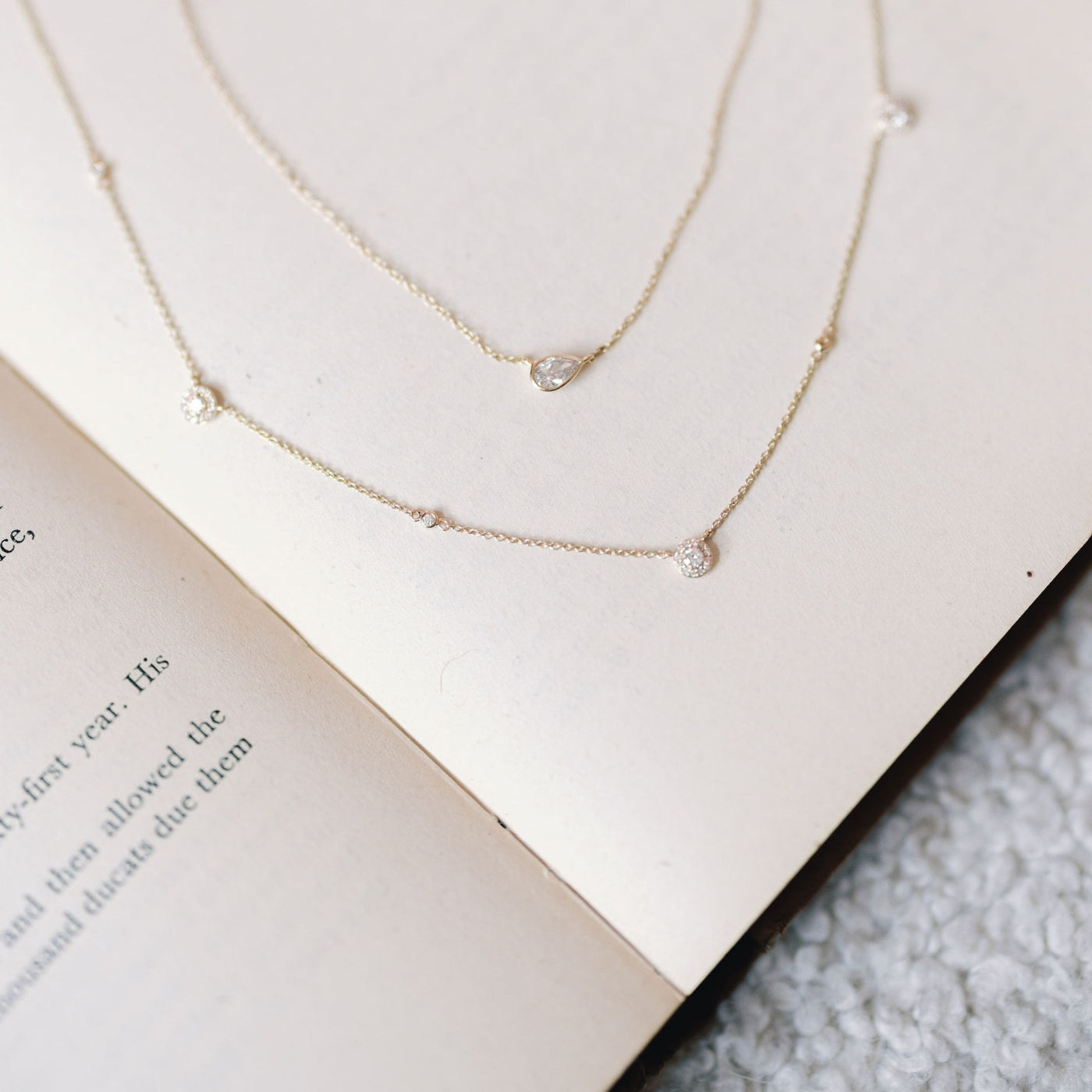 Pear-fect Solitaire Necklace and All That Sparkles Diamond Necklace with lab-grown diamonds on 14K gold chains by Seema Jewelry & Co, elegantly displayed on an open book.