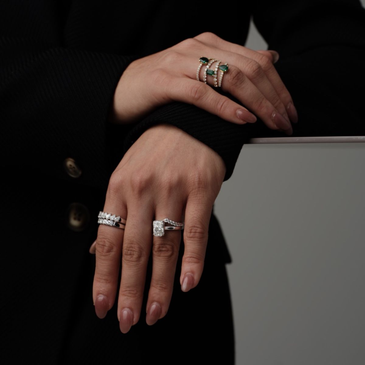 Close-up of hands wearing diamond and green gemstone rings by Seema Jewelry and Co.